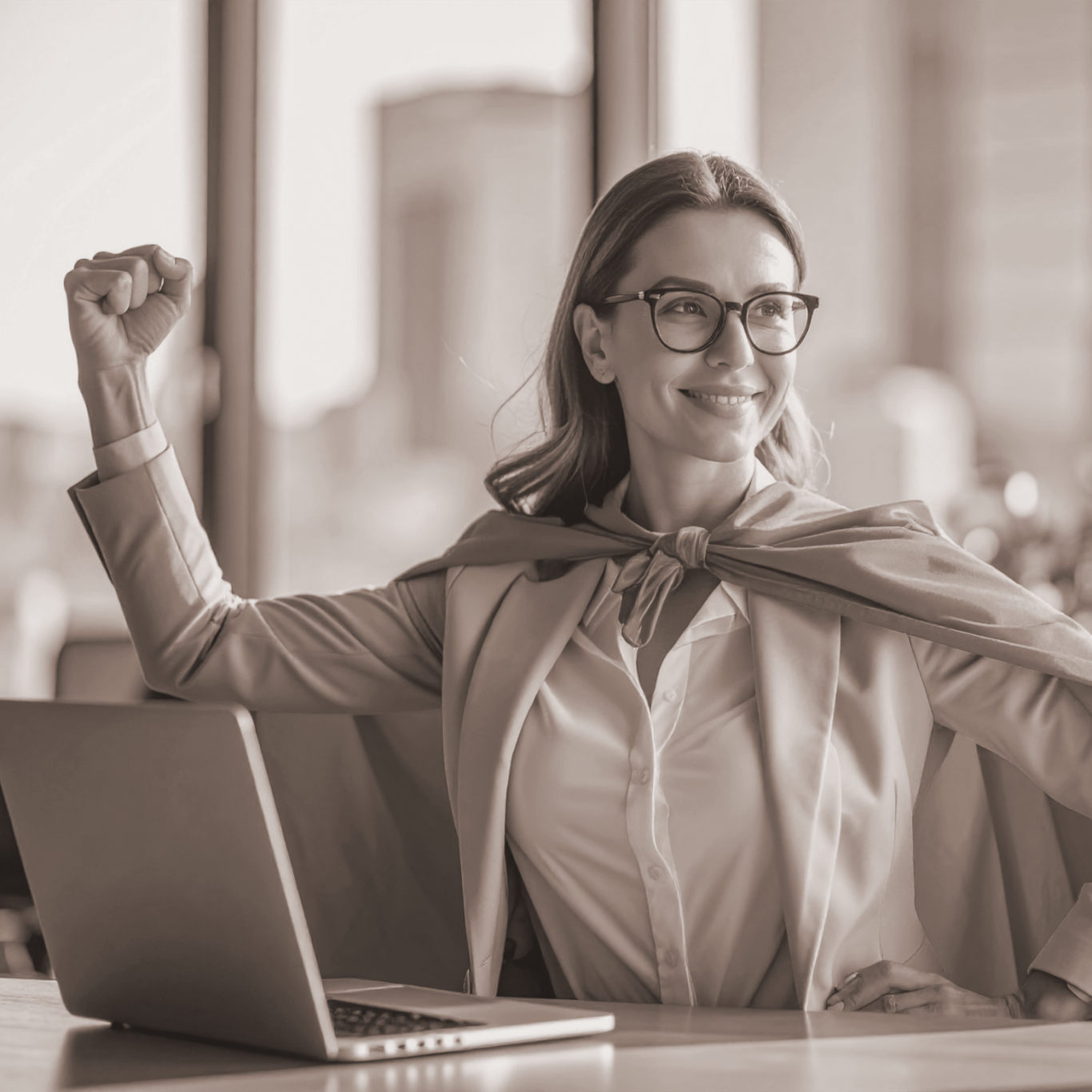 Frau in Anzug mit rotem Umhang, triumphierend vor einem Laptop am Schreibtisch.